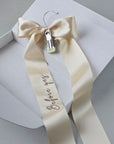 Wedding veil hanger with "Before yes" embroidery on an champagne satin bow, shown in a white gift box.