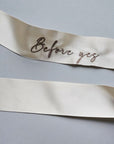 Close-up of the "Before yes" script embroidery on luxury double-faced champagne color satin ribbon for a wedding veil clip.