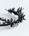 Detailed shot of matte black laurel leaves and dark Swarovski pearls on the LZZY gothic headpiece.