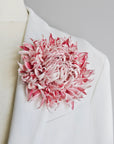 A large, textured pink and soft white silk flower brooch pinned to the lapel of a white suit jacket on a mannequin torso.