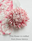 A pink and soft white silk fabric chrysanthemum flower on a white background next to a matching patterned fabric swatch, with text reading 'This flower is crafted from these fabrics'.