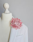 Large blush pink silk flower brooch worn on a white bridal coat lapel