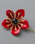 Red enamel poppy flower lapel pin with glossy petals, brass details and black center