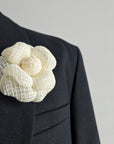White floral brooch on a dark suit jacket against a gray background