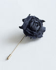 Black velvet rose boutonniere on metal stick, minimalist dark botanical accessory on white background