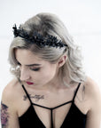 Profile view of a bride with blonde wavy hair and a skull tattoo wearing the LZZY black gothic tiara against a white brick wall.