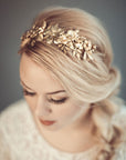 Thalia gold botanical bridal headband featuring dense handcrafted brass leaves and wildflowers with Preciosa pearls, shown on a bride with a blonde side-braid.