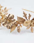 Close-up of THALIA bridal headband on a white linen surface, showcasing the intricate layers of gold-tone matte brass wildflowers, heritage leaves, and Preciosa pearl centers.