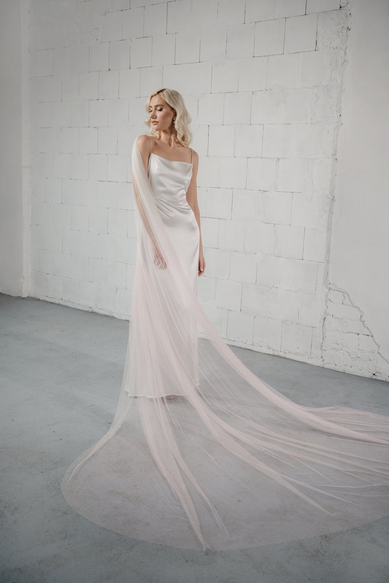 Bride wearing the Phila Cape Veil with a blush ombre effect, draping elegantly over her ivory wedding gown. A chic and unique alternative to a traditional veil.