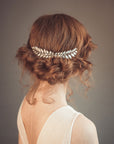 Bride wearing a Grecian-inspired laurel hair comb with hand-enameled soft white leaves, pearls, and crystal accents, styled in a soft bridal updo