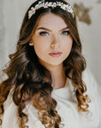 Victoria hand-painted white leaf bridal tiara on a brunette bride with long wavy hair, showcasing the sculptural vine silhouette and matte botanical finish against a textured wall background.