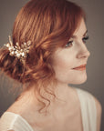 Side profile of a bride with red hair and a low bun wearing the TYCHE gold leaf hair vine comb with pearls for a vintage-inspired bridal look.