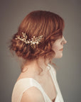Side profile of a bride with red hair and a low bun wearing the TYCHE gold leaf hair vine comb with pearls for a vintage-inspired bridal look.