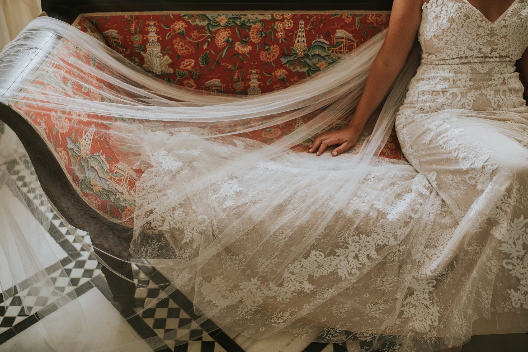 bride sitting on red vintage sofa. Bride wear soft tulle veil.