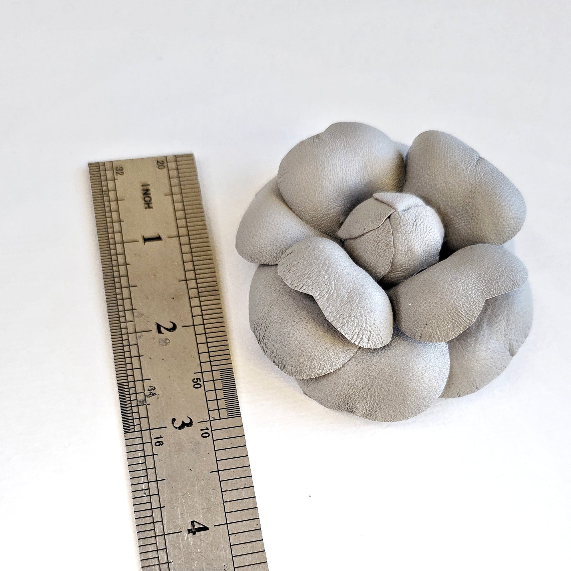 Gray leather caellia brooch next to a ruler on a white background
