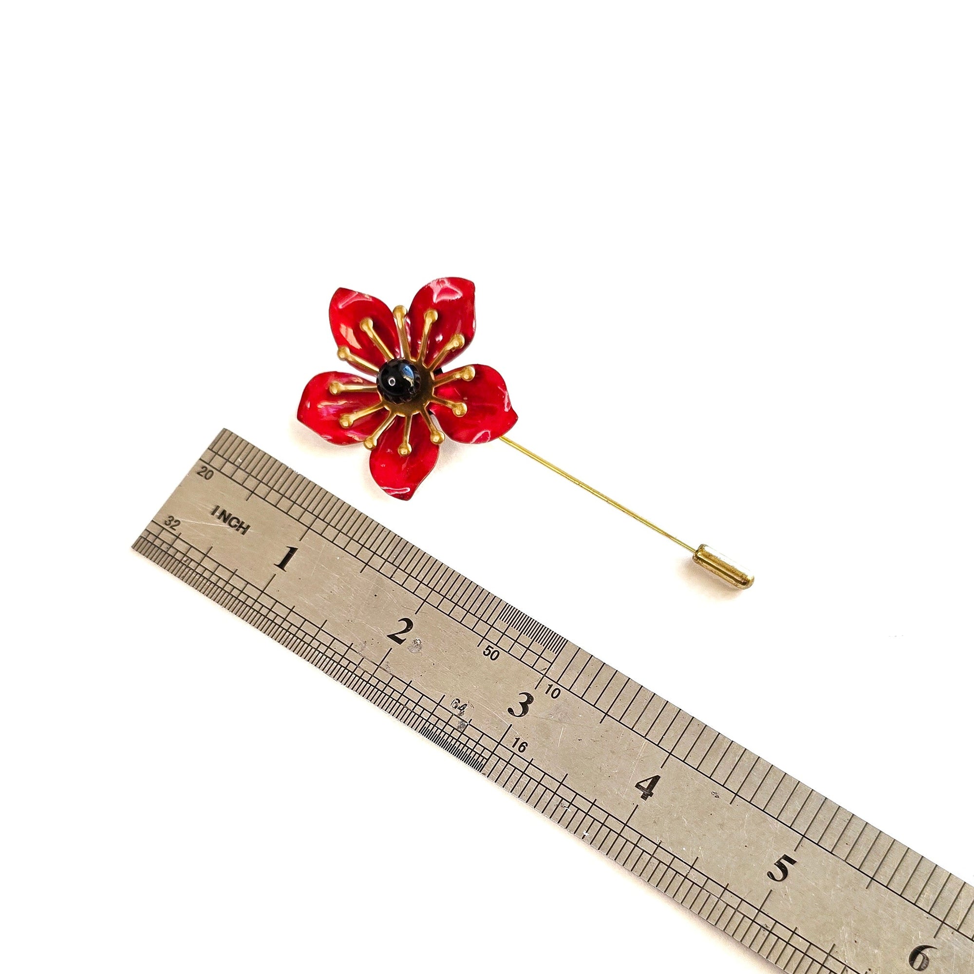 Red poppy lapel pin next to ruler showing flower size and total pin length