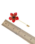 Red poppy lapel pin next to ruler showing flower size and total pin length