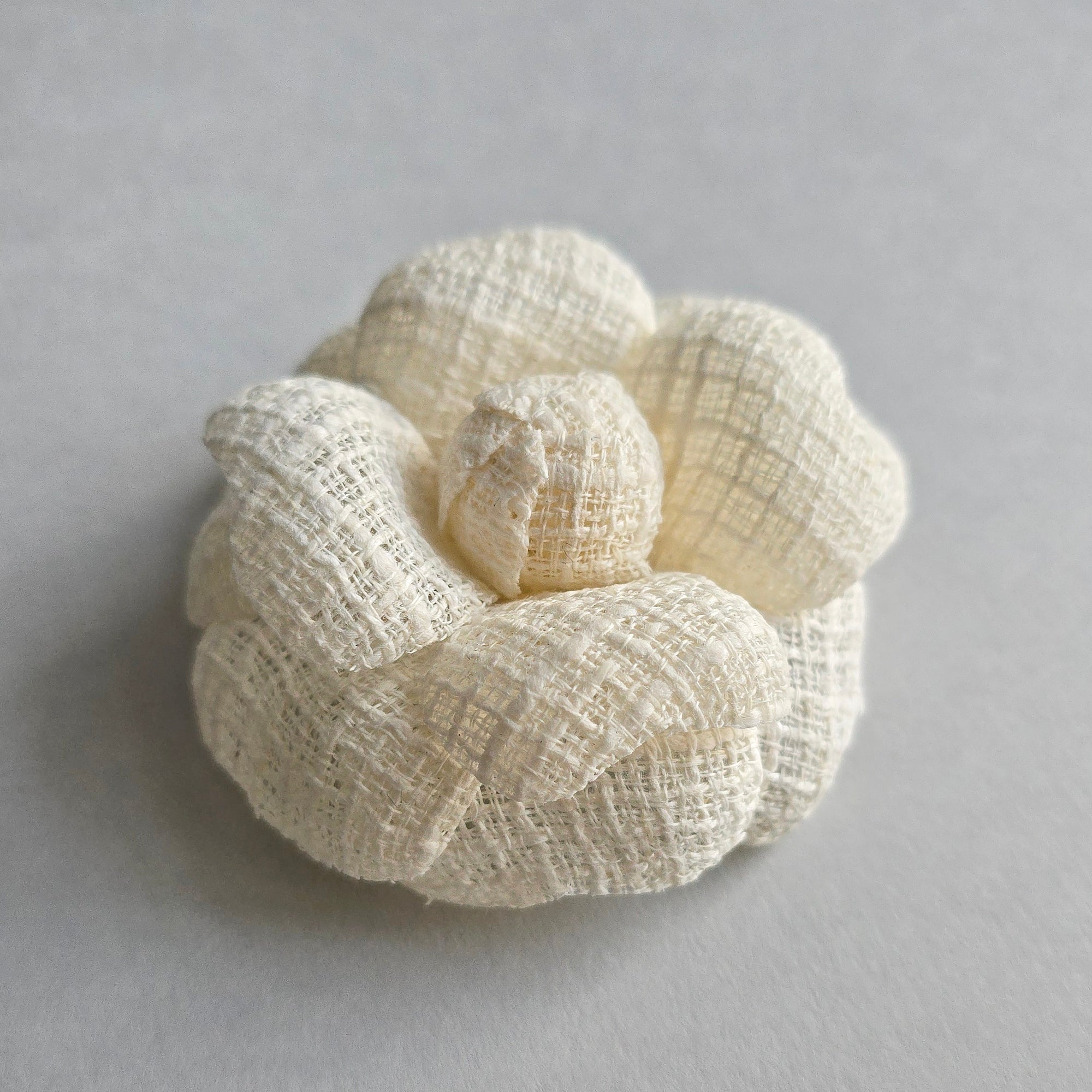Ivory tweed camellia brooch pin on light background, elegant wedding accessory
