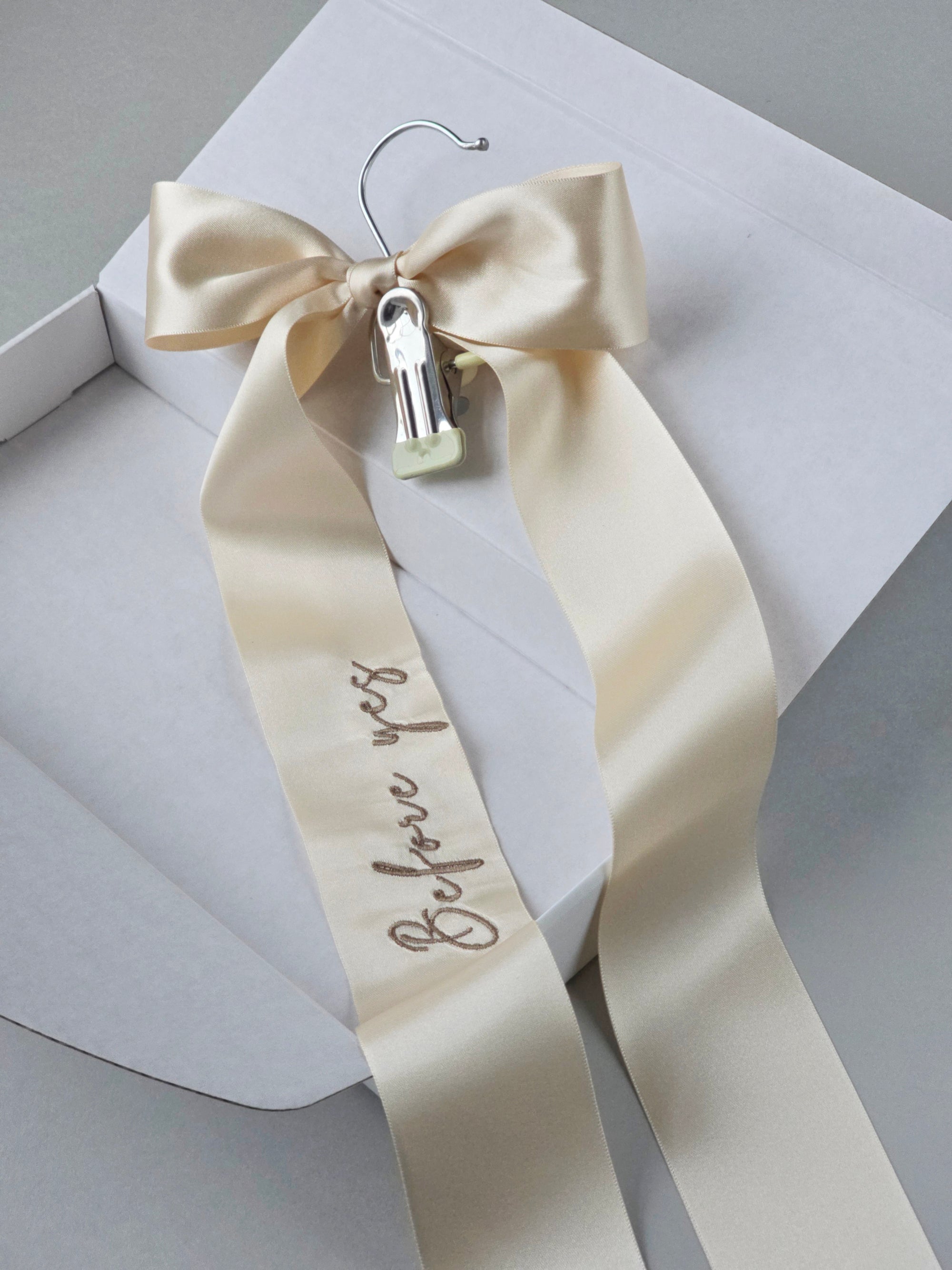 Wedding veil hanger with "Before yes" embroidery on an champagne satin bow, shown in a white gift box.