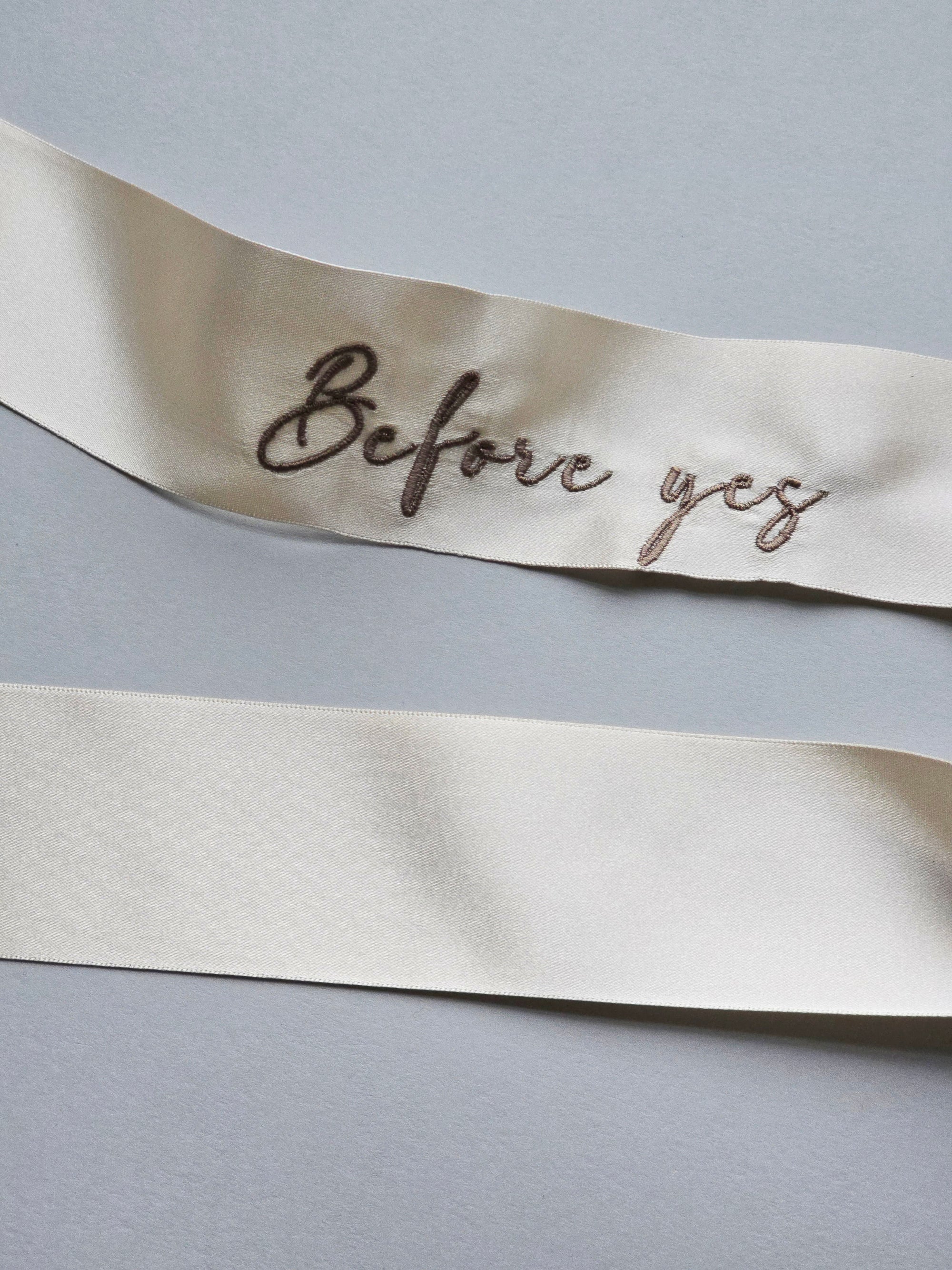 Close-up of the "Before yes" script embroidery on luxury double-faced champagne color satin ribbon for a wedding veil clip.