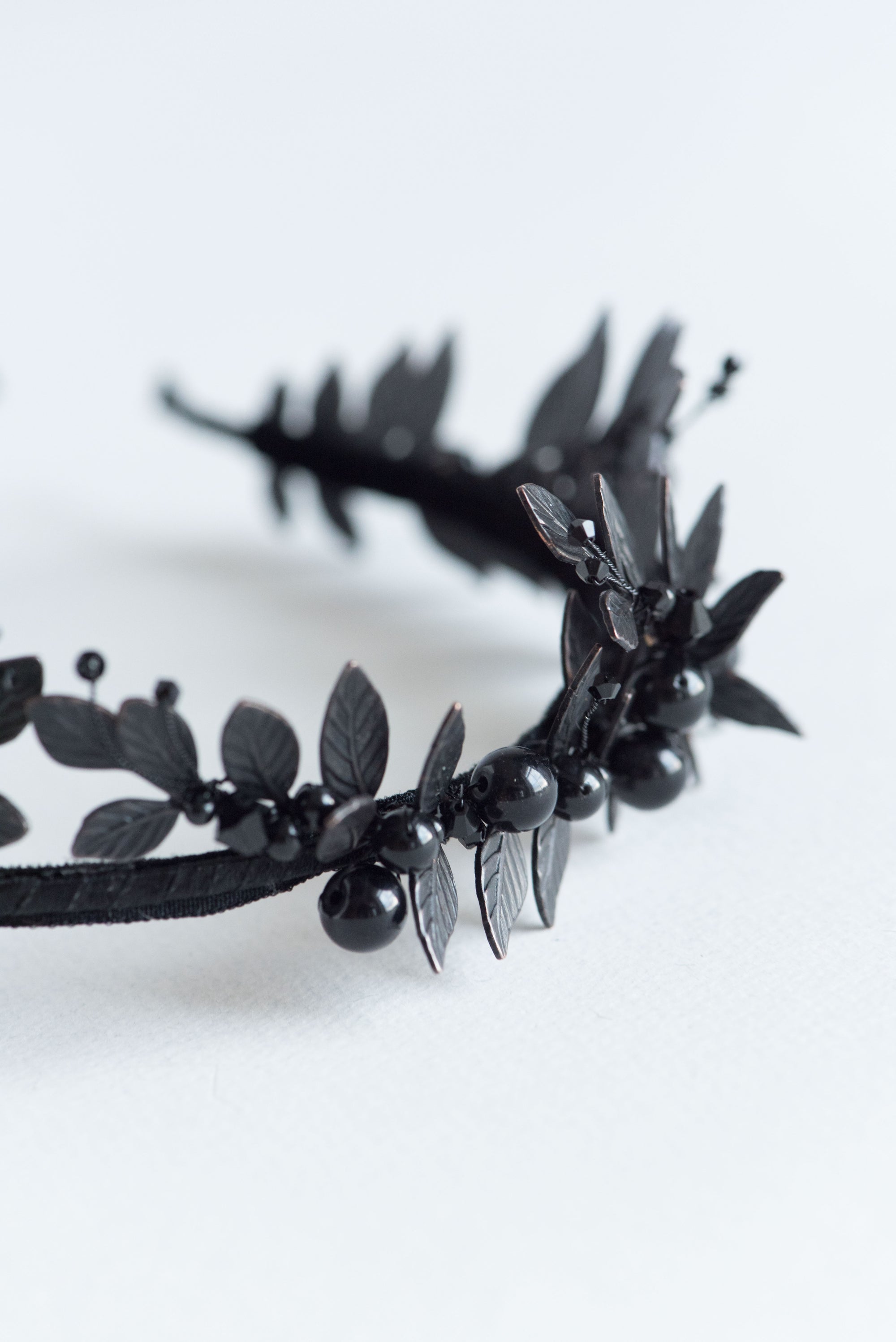 Detailed shot of matte black laurel leaves and dark Swarovski pearls on the LZZY gothic headpiece.