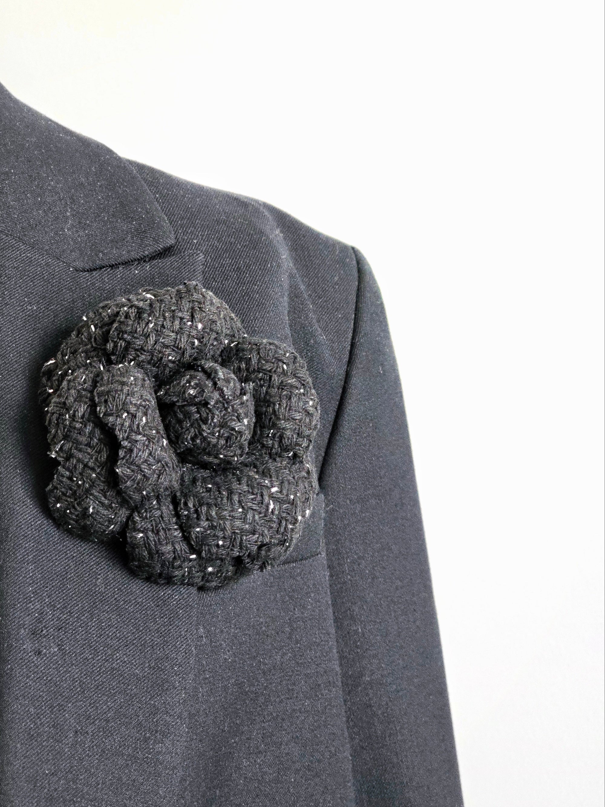 Handmade black tweed camellia flower pin with silver metallic shimmer styled on a black blazer, Dark Romance aesthetic.