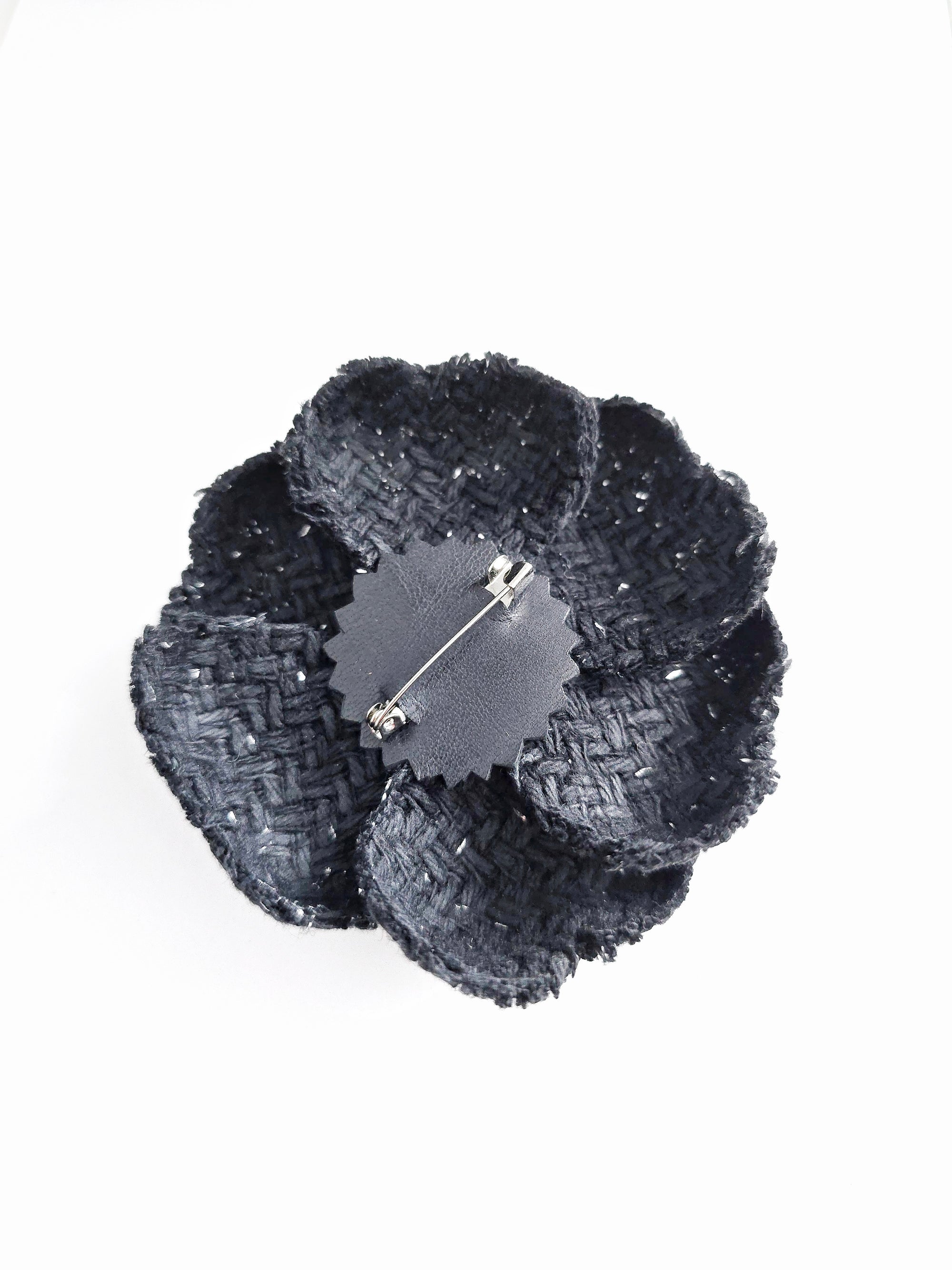 The back view of a black tweed camellia brooch showing a secure silver-tone metal pin attachment for easy fastening to clothing
