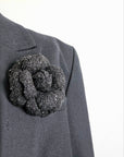 Handmade black tweed camellia flower pin with silver metallic shimmer styled on a black blazer, Dark Romance aesthetic.