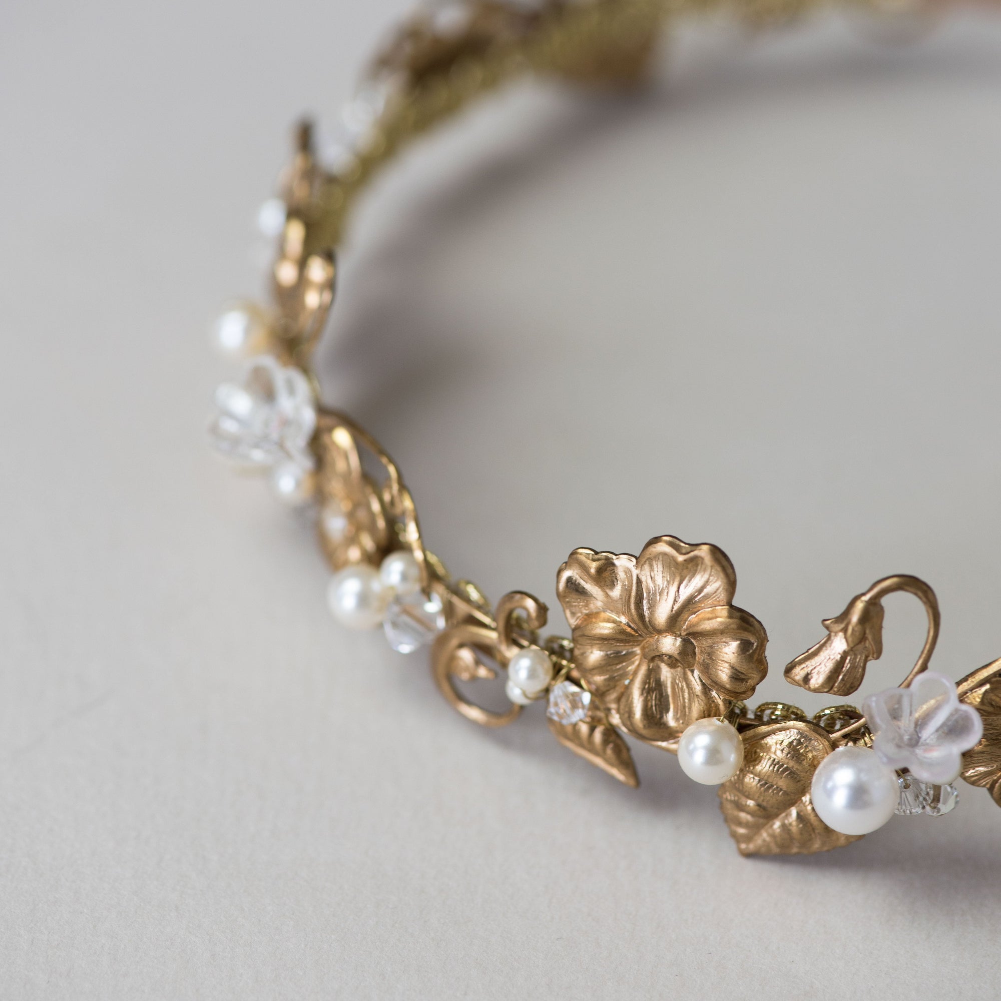 Gold headband with floral and leaf designs on a light gray background