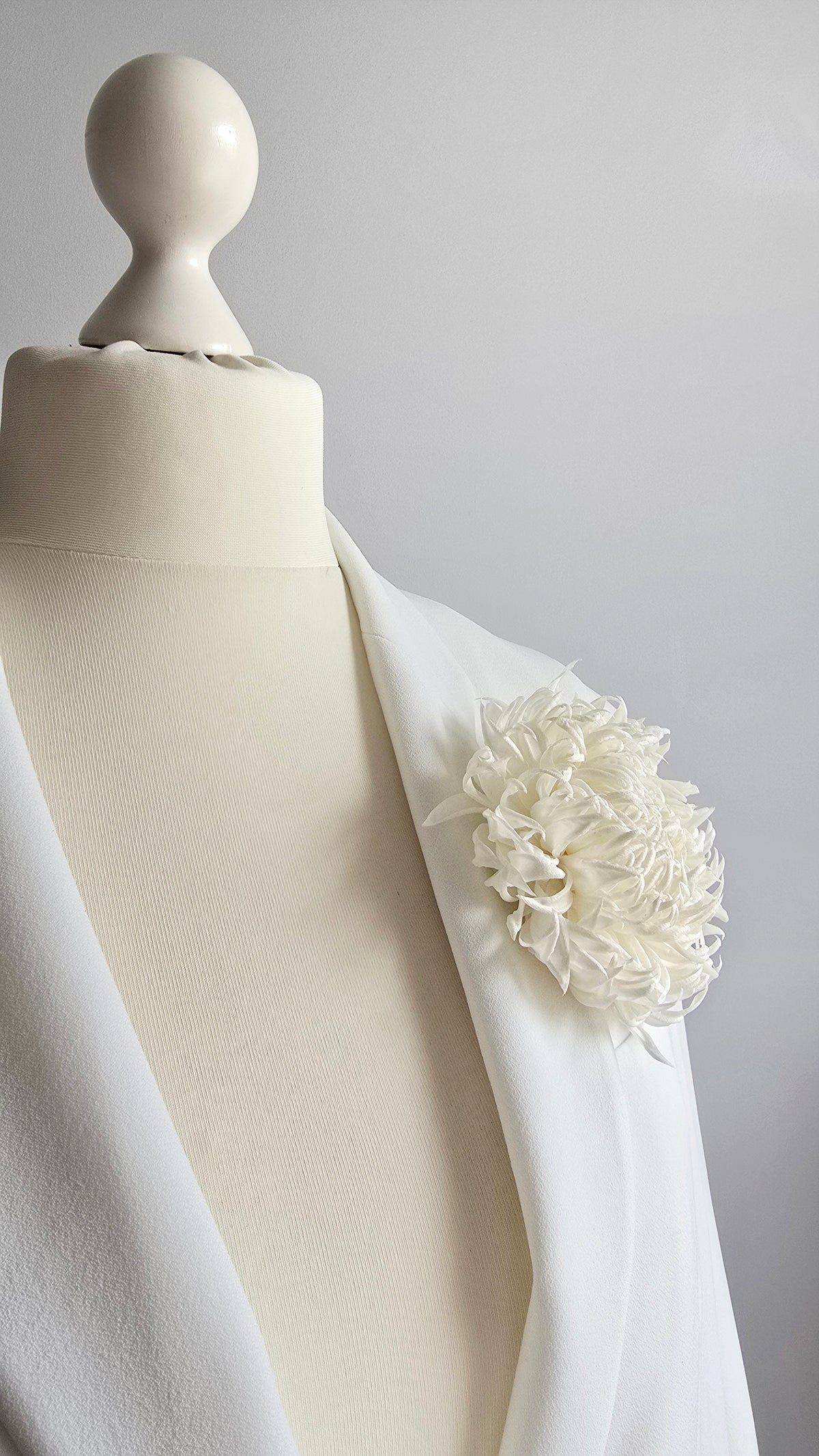 Side view of pure ivory silk chrysanthemum statement pin styled on white bridal coat