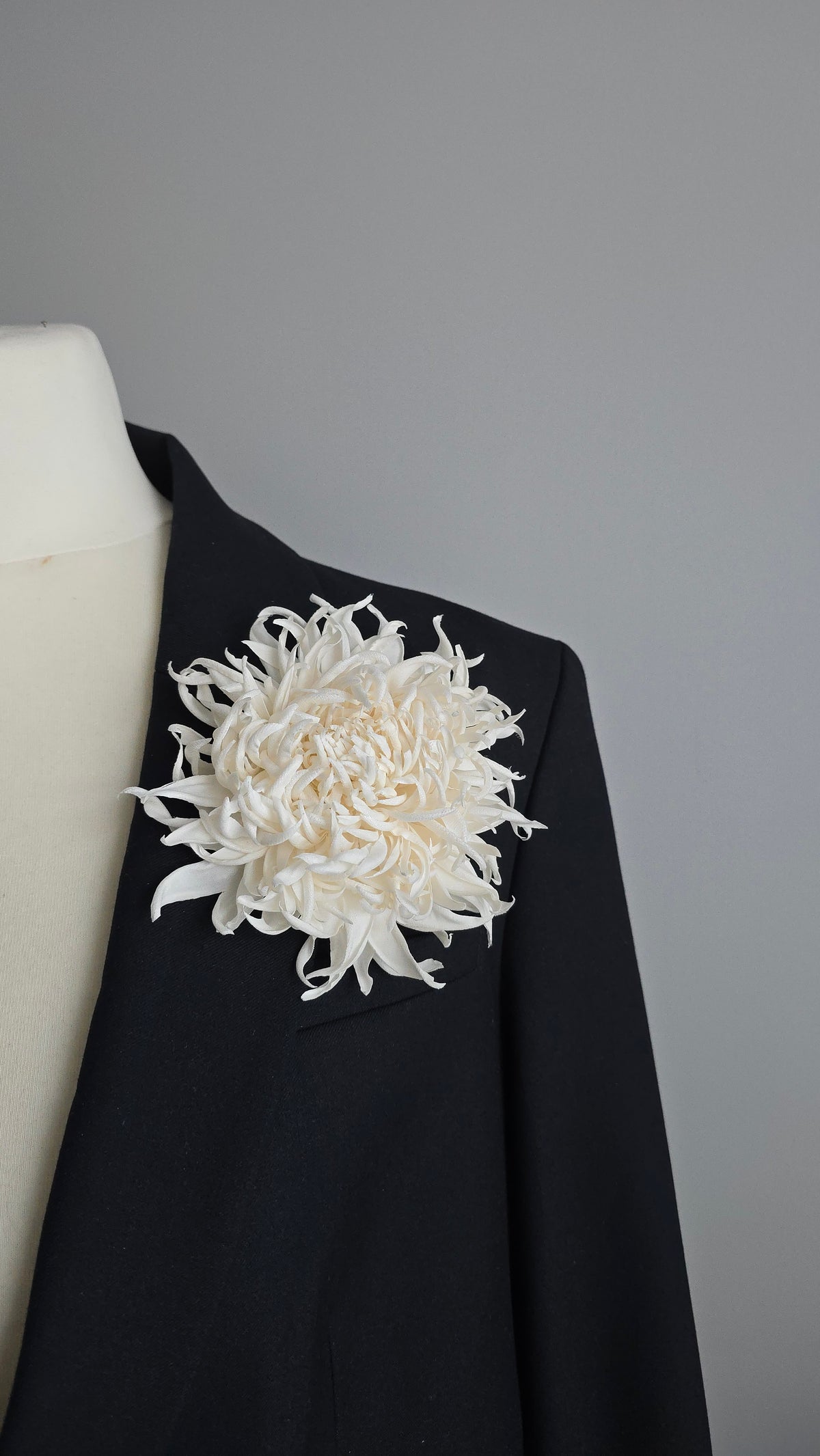 Pure ivory silk chrysanthemum brooch styled on a dark black blazer lapel for contrast
