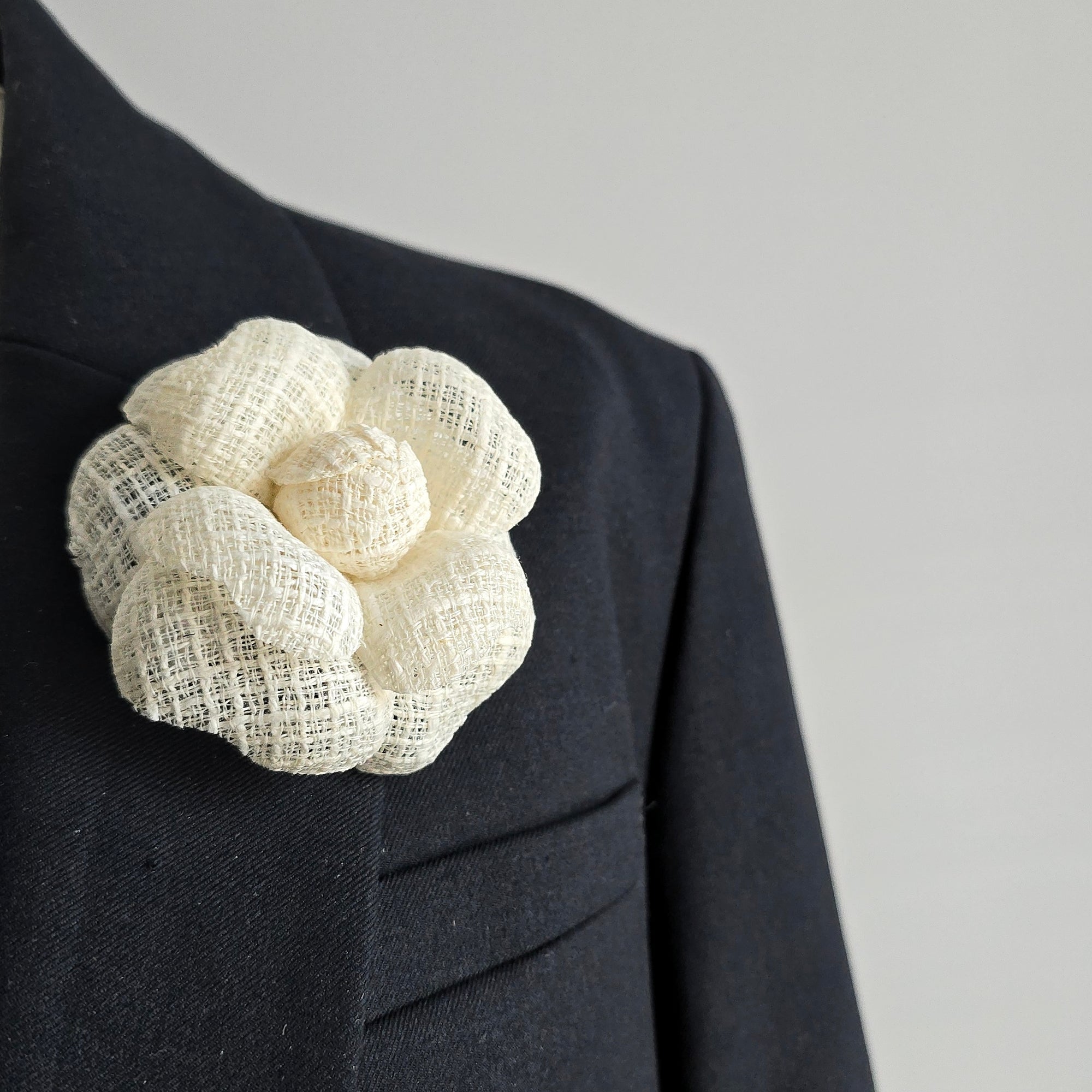 White floral brooch on a dark suit jacket against a gray background
