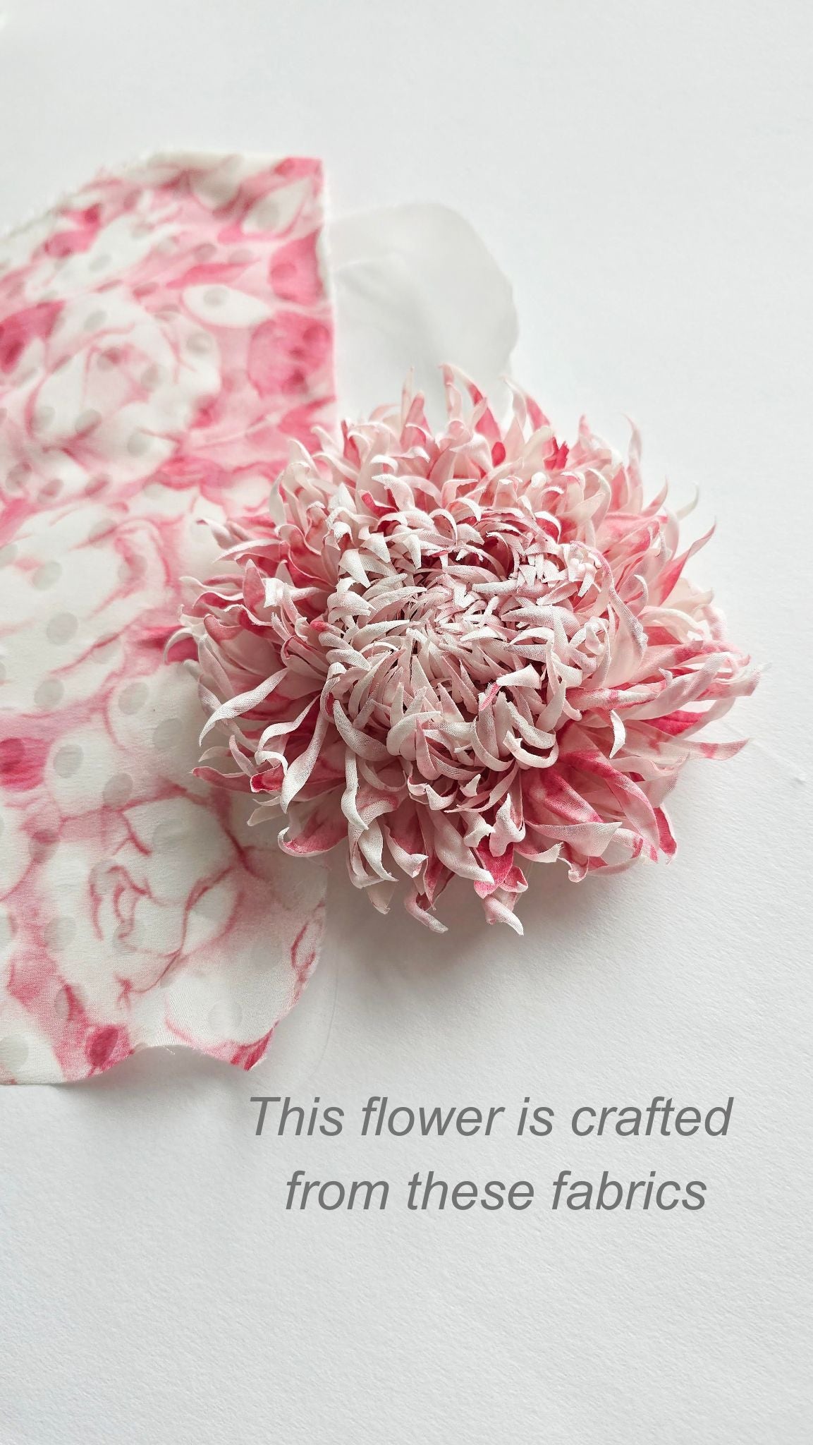 A pink and soft white silk fabric chrysanthemum flower on a white background next to a matching patterned fabric swatch, with text reading 'This flower is crafted from these fabrics'.