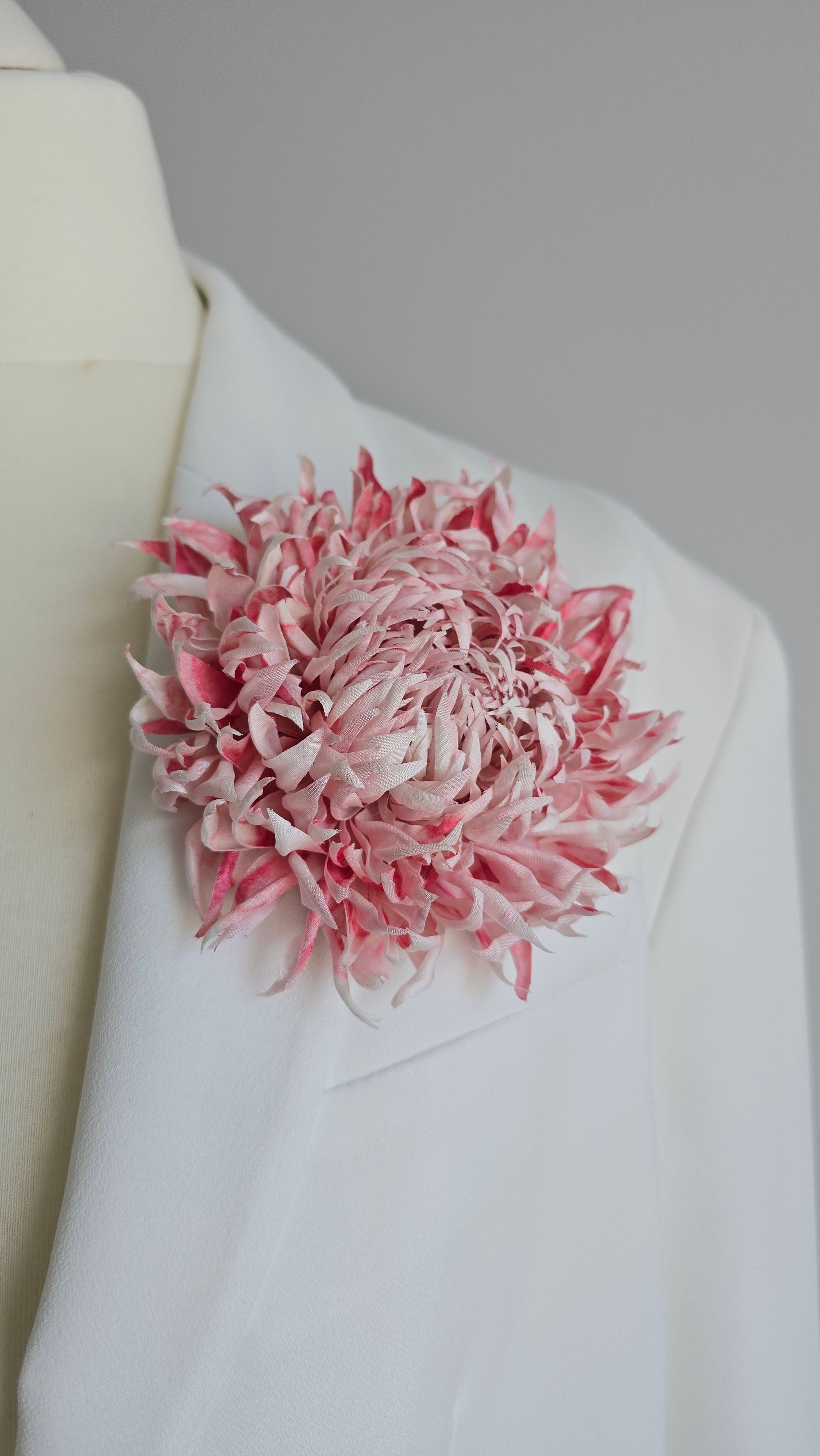 Large blush pink silk flower brooch worn on a white bridal coat lapel.
