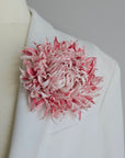 Large blush pink silk flower brooch worn on a white bridal coat lapel.