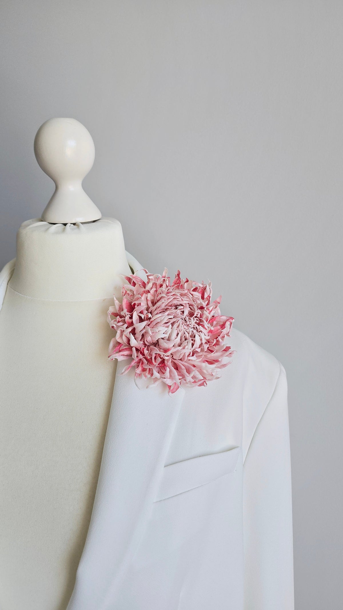 Large blush pink silk flower brooch worn on a white bridal coat lapel