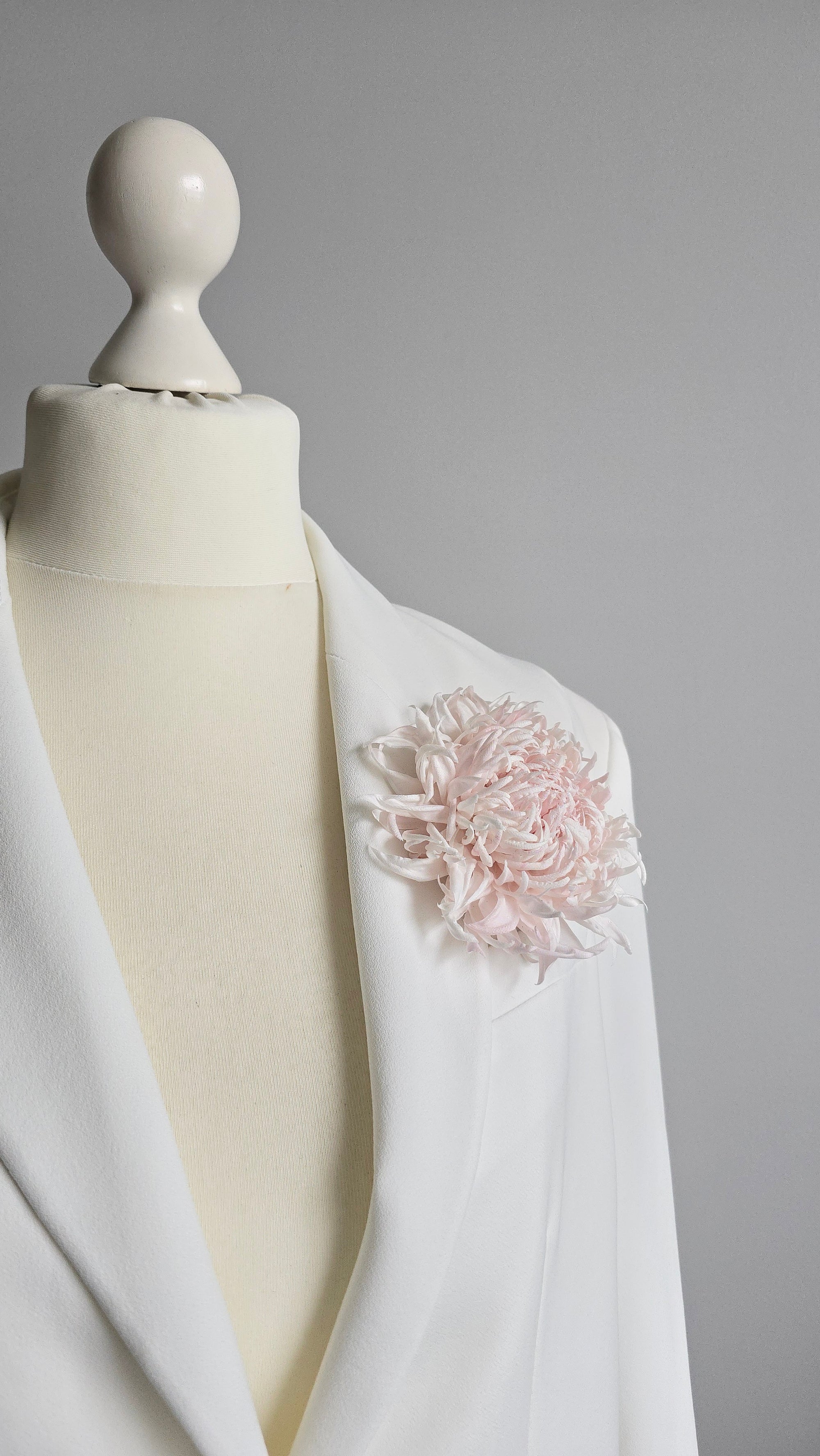 Handcrafted powder pink silk chrysanthemum brooch pinned on a white blazer lapel