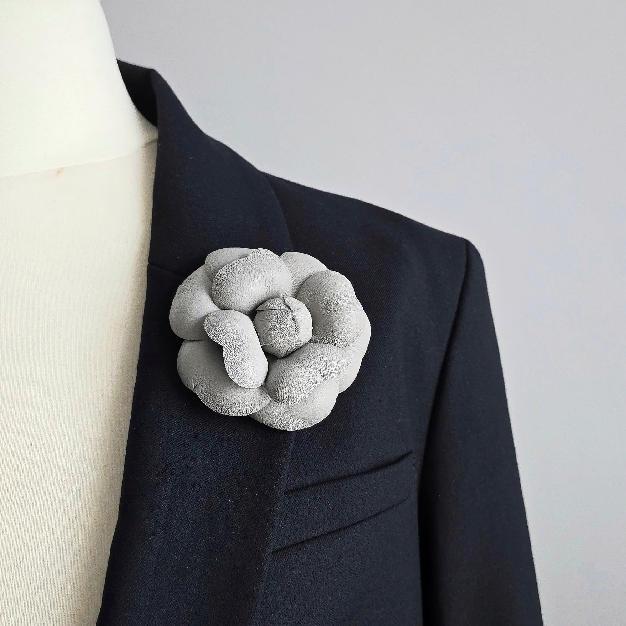 Grey  leather camellia brooch worn on black blazer showing scale and styling