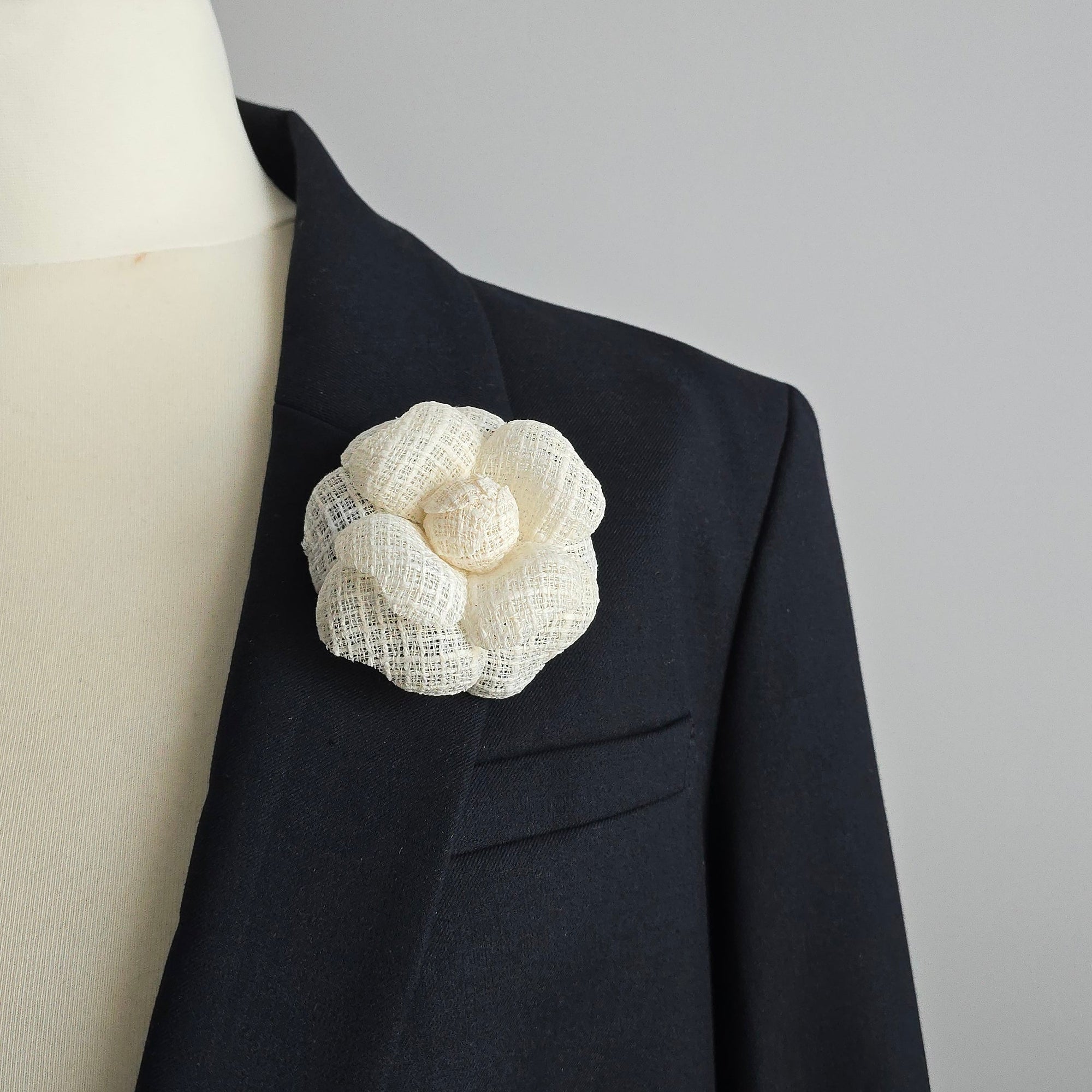 Ivory tweed camellia flower brooch pin detail on a mannequin against a gray background
