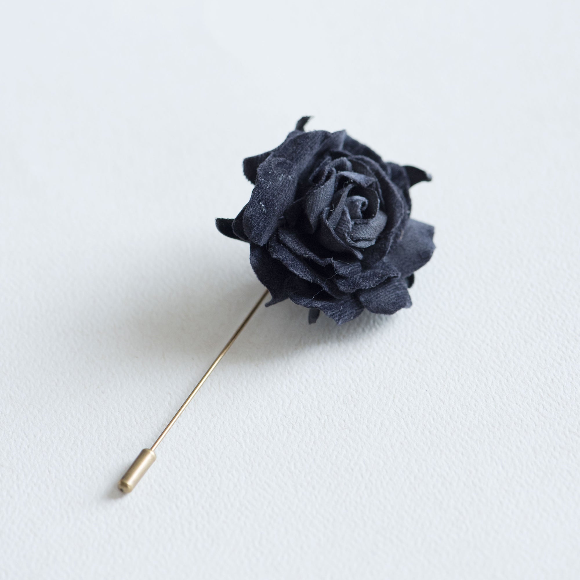Black velvet rose boutonniere on metal stick, minimalist dark botanical accessory on white background
