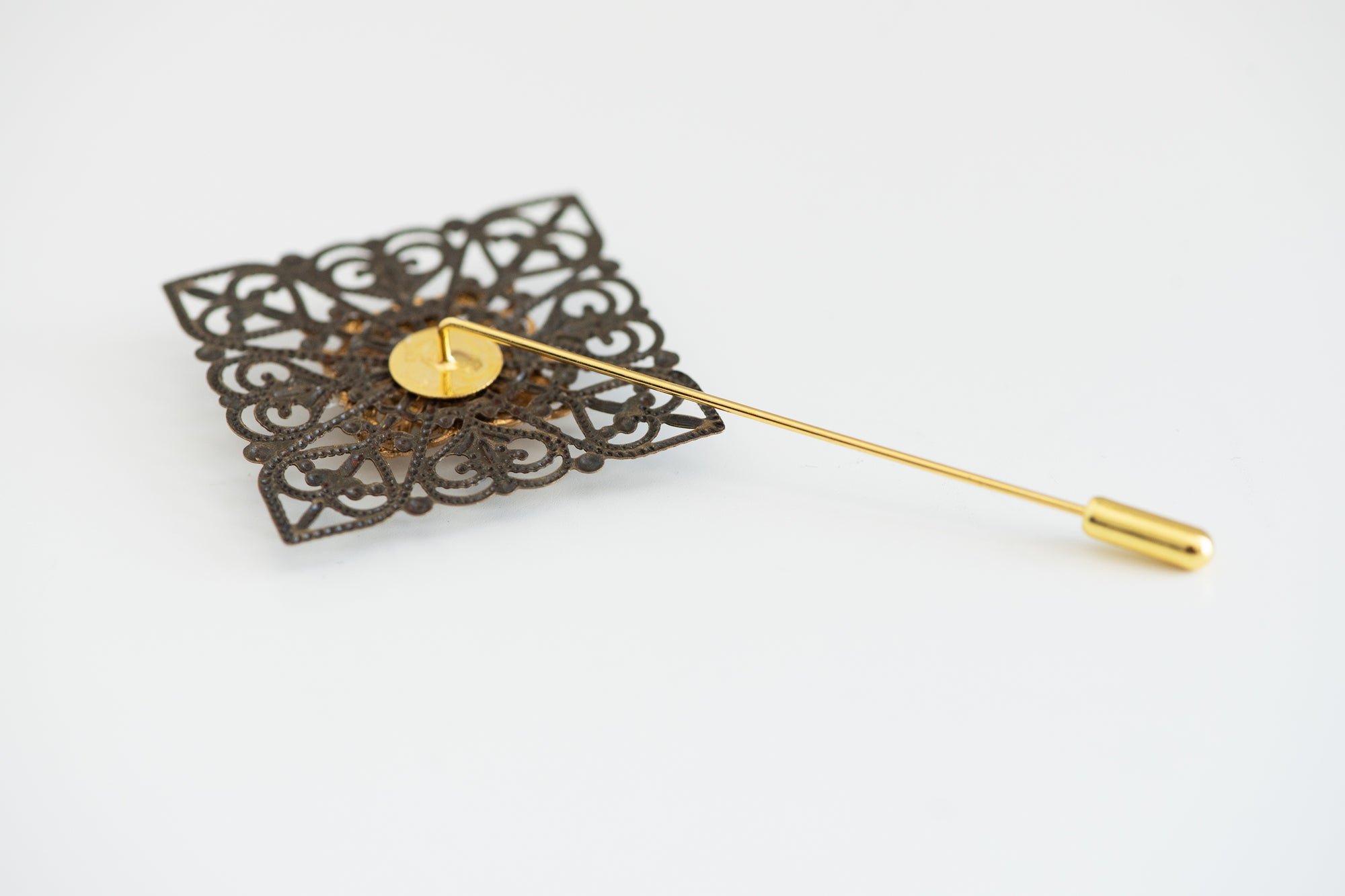 Handmade brass groom boutonniere on white background with filigree detailing