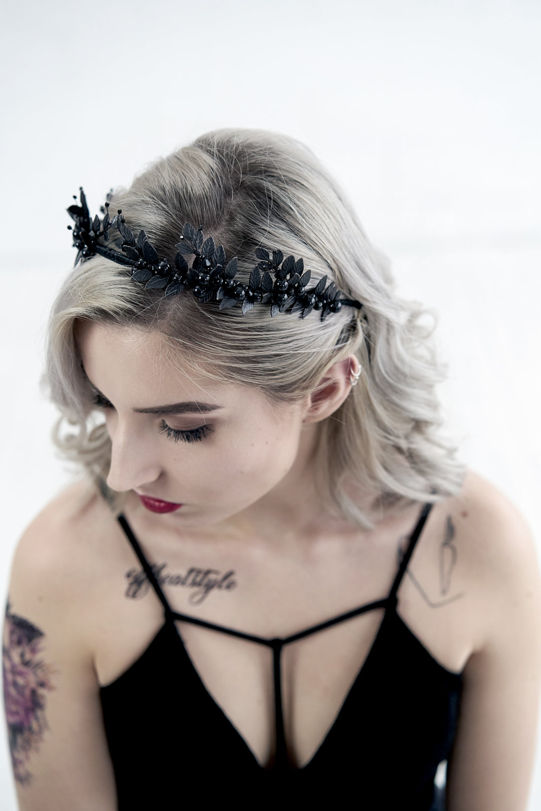Profile view of a bride with blonde wavy hair and a skull tattoo wearing the LZZY black gothic tiara against a white brick wall.