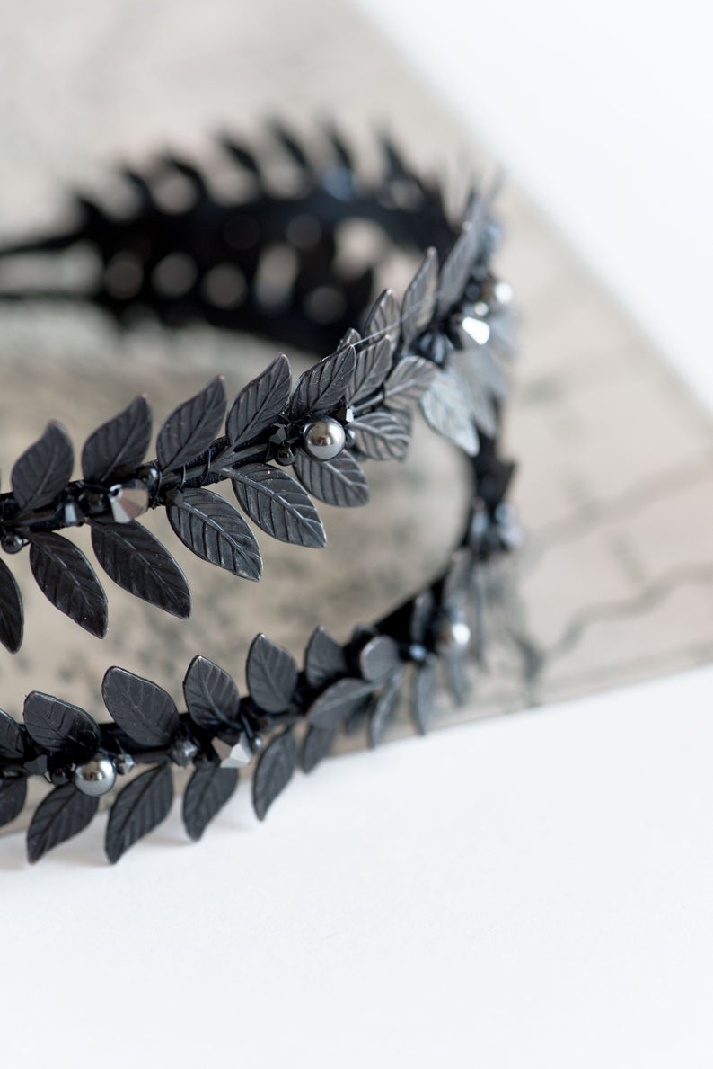 Close-up of MARIA black laurel leaf tiara resting on an antique open book, showing the matte black brass leaves and dark pearls.
