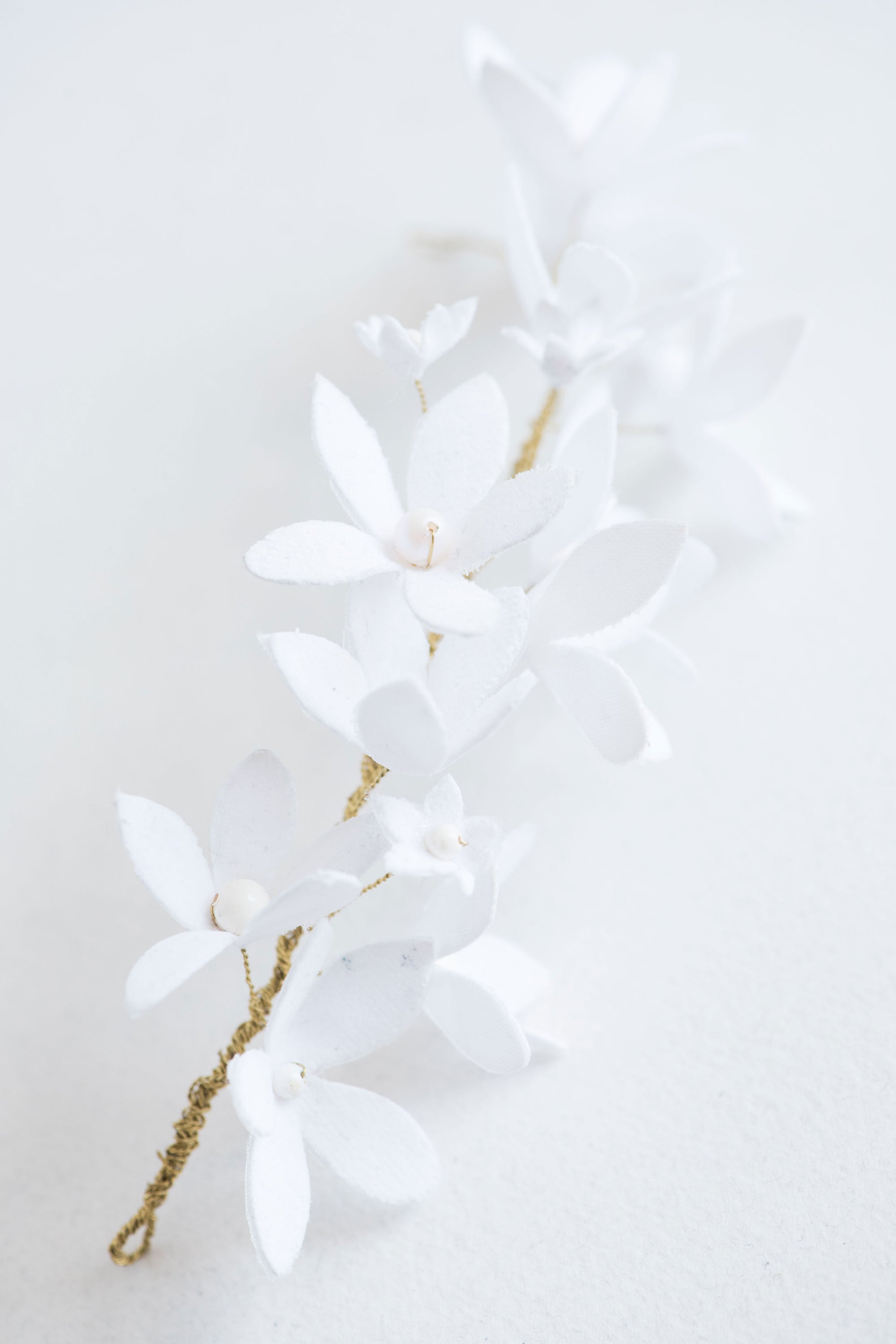Close-up of handmade bridal hair vine with white blossoms and gold wire