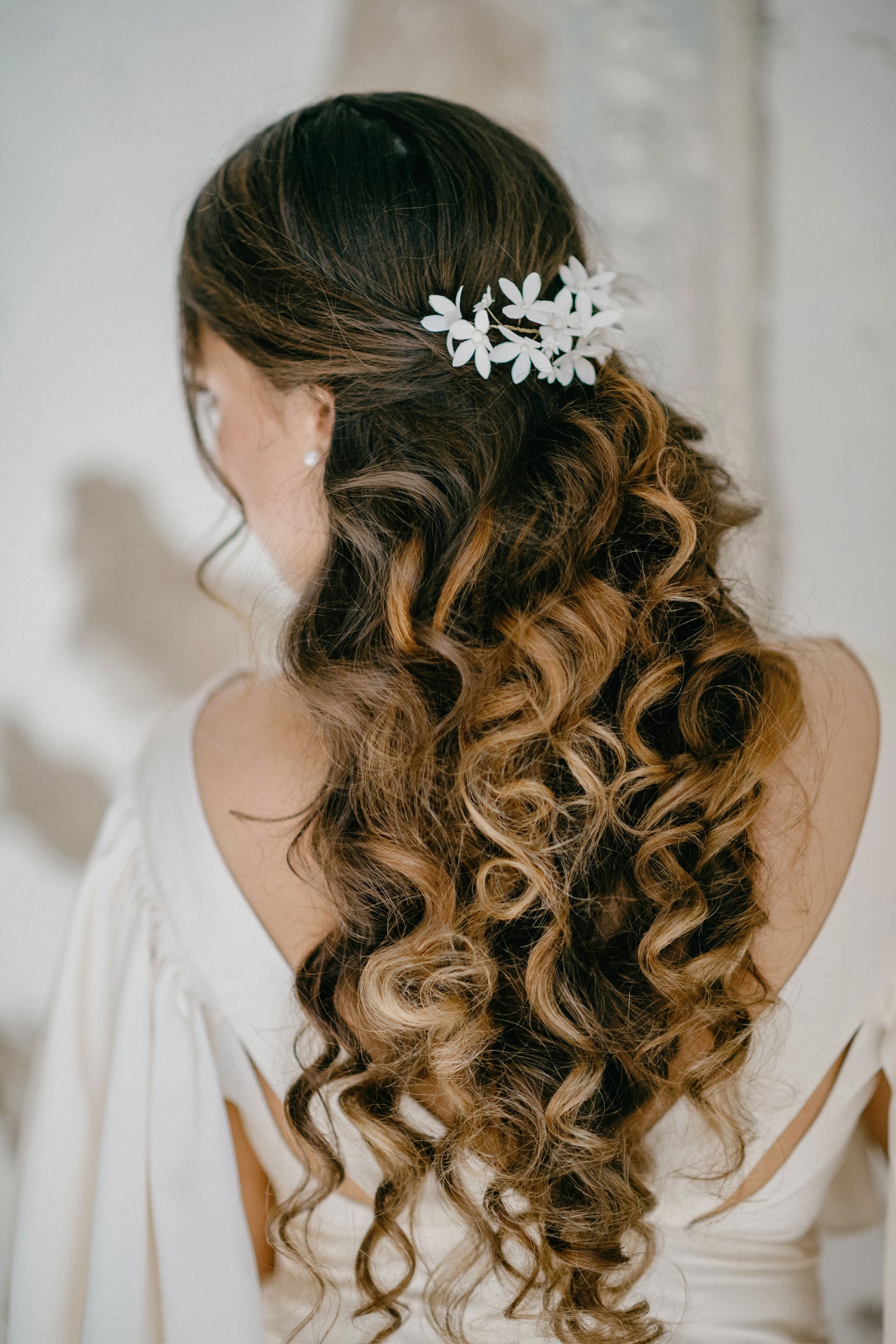 A bride with long brunette curls wearing the LIUCINA white velvet jasmine hair vine, demonstrating how the flexible floral vine shapes around a half-up bridal hairstyle.