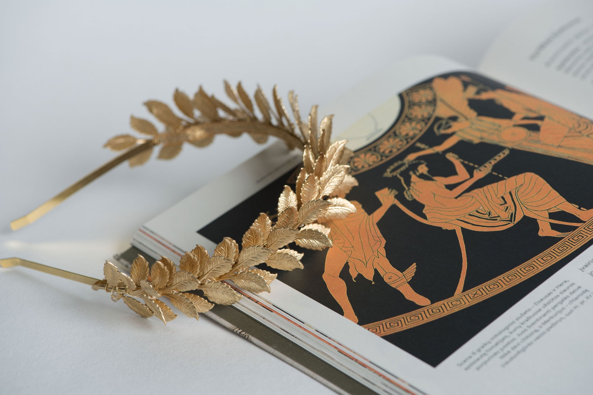 CLOTILDE gold wedding headband resting on mythology book – Roman inspired design