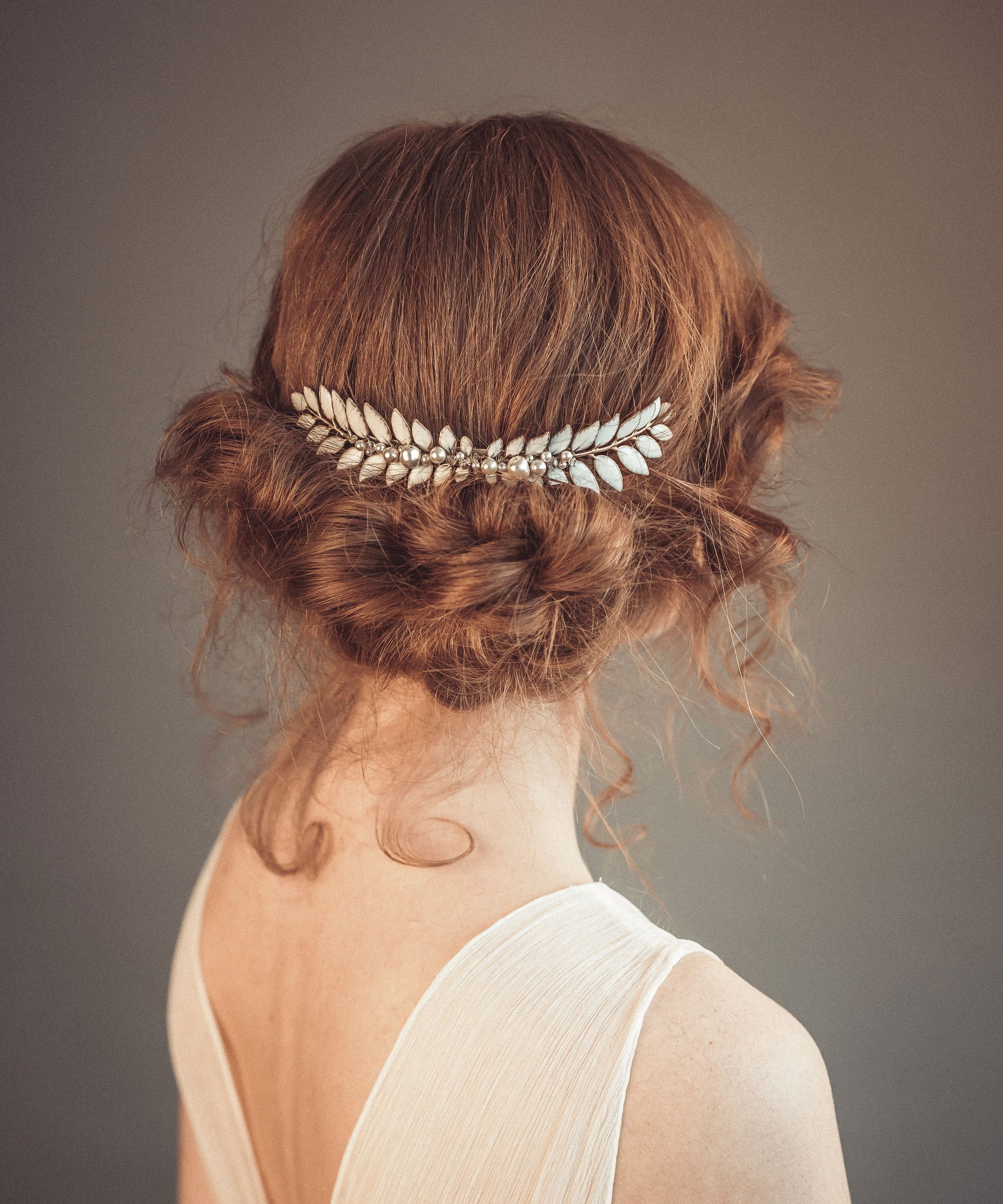 Bride wearing a Grecian-inspired laurel hair comb with hand-enameled soft white leaves, pearls, and crystal accents, styled in a soft bridal updo