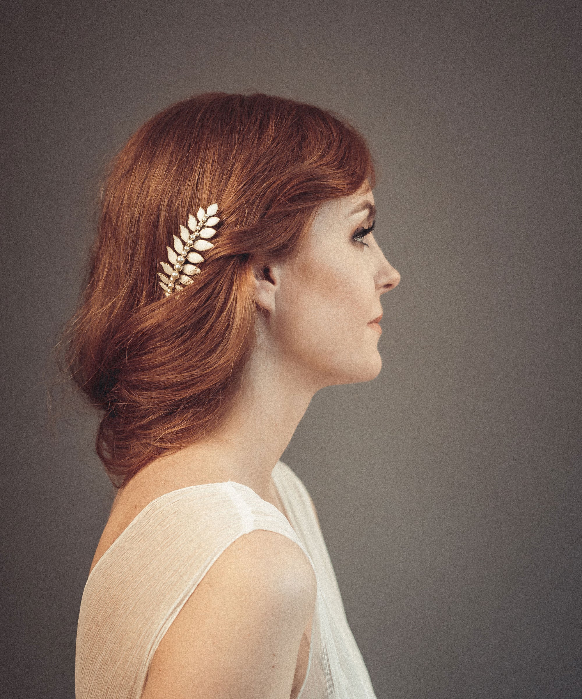 Gold laurel leaf hair comb with off-white enamel and pearl accents worn in a loose bridal updo