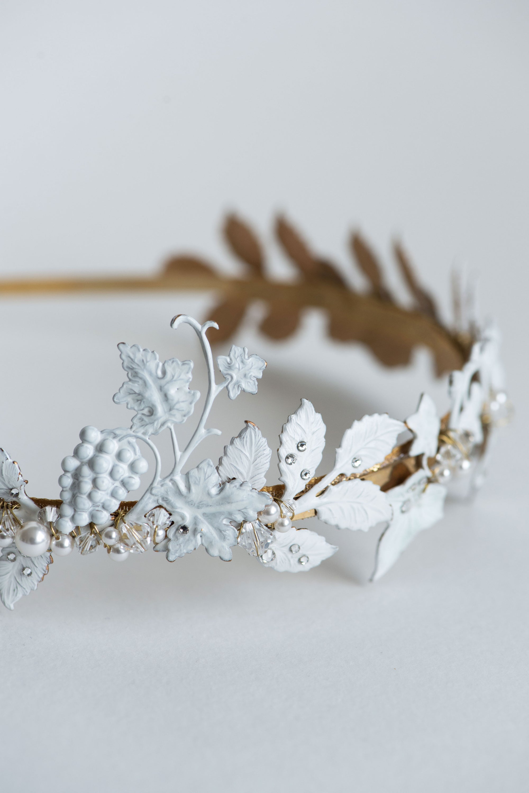Detailed close-up of the VICTORIA bridal tiara featuring hand-painted white matte leaves, golden vine structure, and pearl accents with Austrian crystals, emphasizing the artisanal lacquer finish.