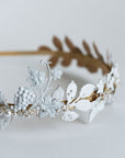 Detailed close-up of the VICTORIA bridal tiara featuring hand-painted white matte leaves, golden vine structure, and pearl accents with Austrian crystals, emphasizing the artisanal lacquer finish.